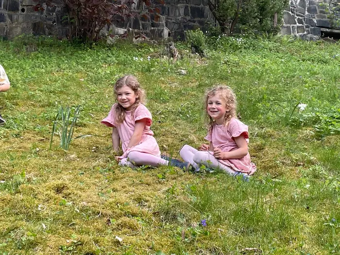 Zwei Kinder sitzen im Gras auf dem Gemeindegelände